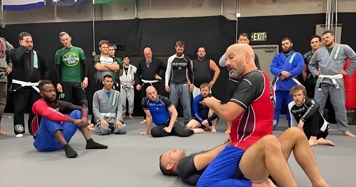A group practices jiu-jitsu. A coach demonstrates a technique while others watch. Training gym setting.