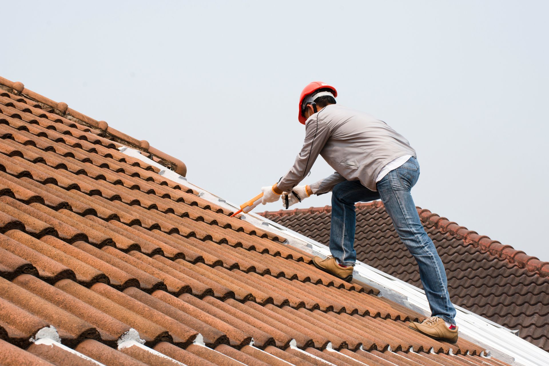 Roofer in hard hat replacing tiles on a clay tile roof. Roofer in hard hat replacing tiles on a clay tile roof.