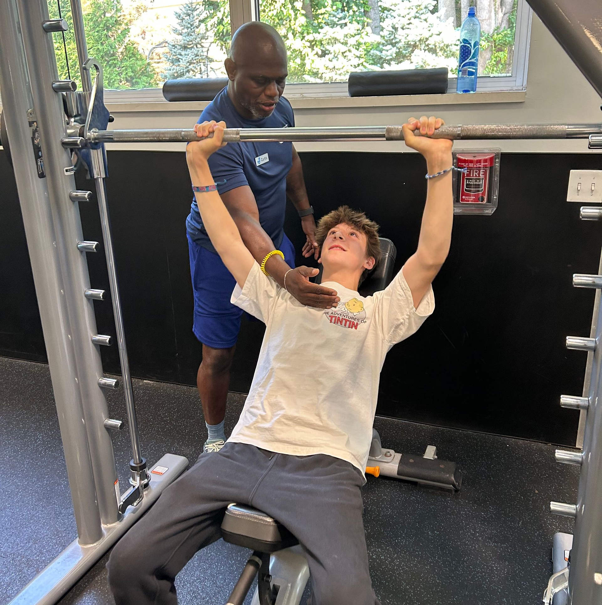 Man spotting a young person doing bench press in a gym.