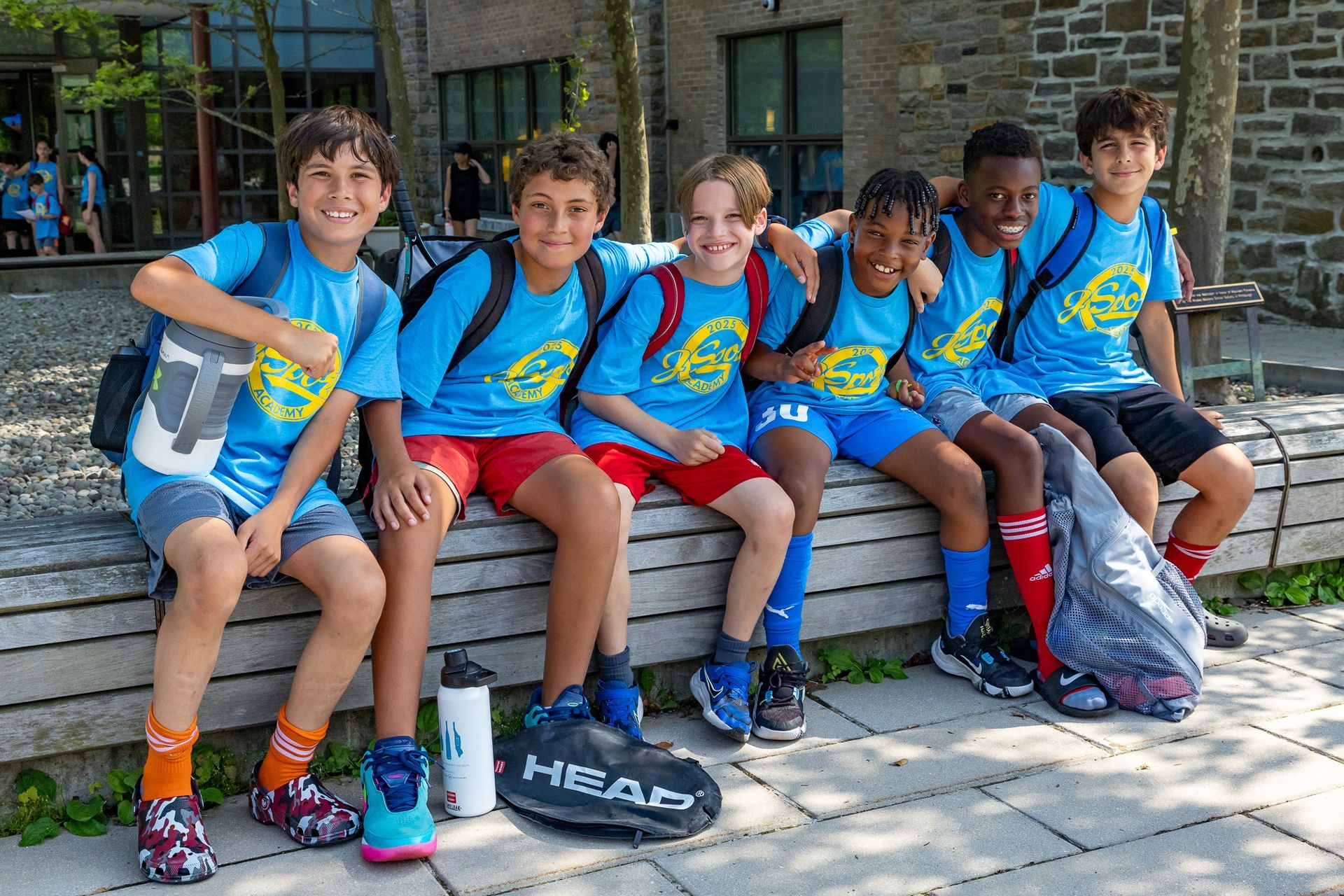 Group of boys in blue shirts, sitting outside, smiling.