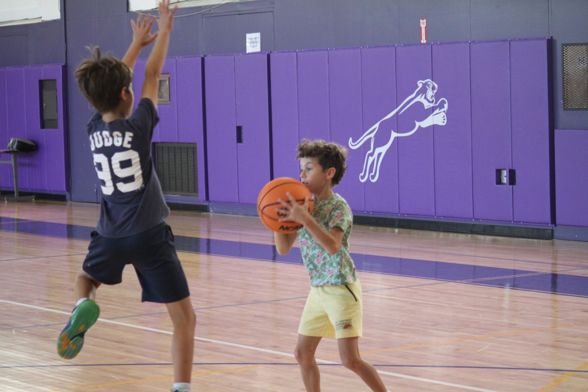 Two young boys are playing basketball in a gym.