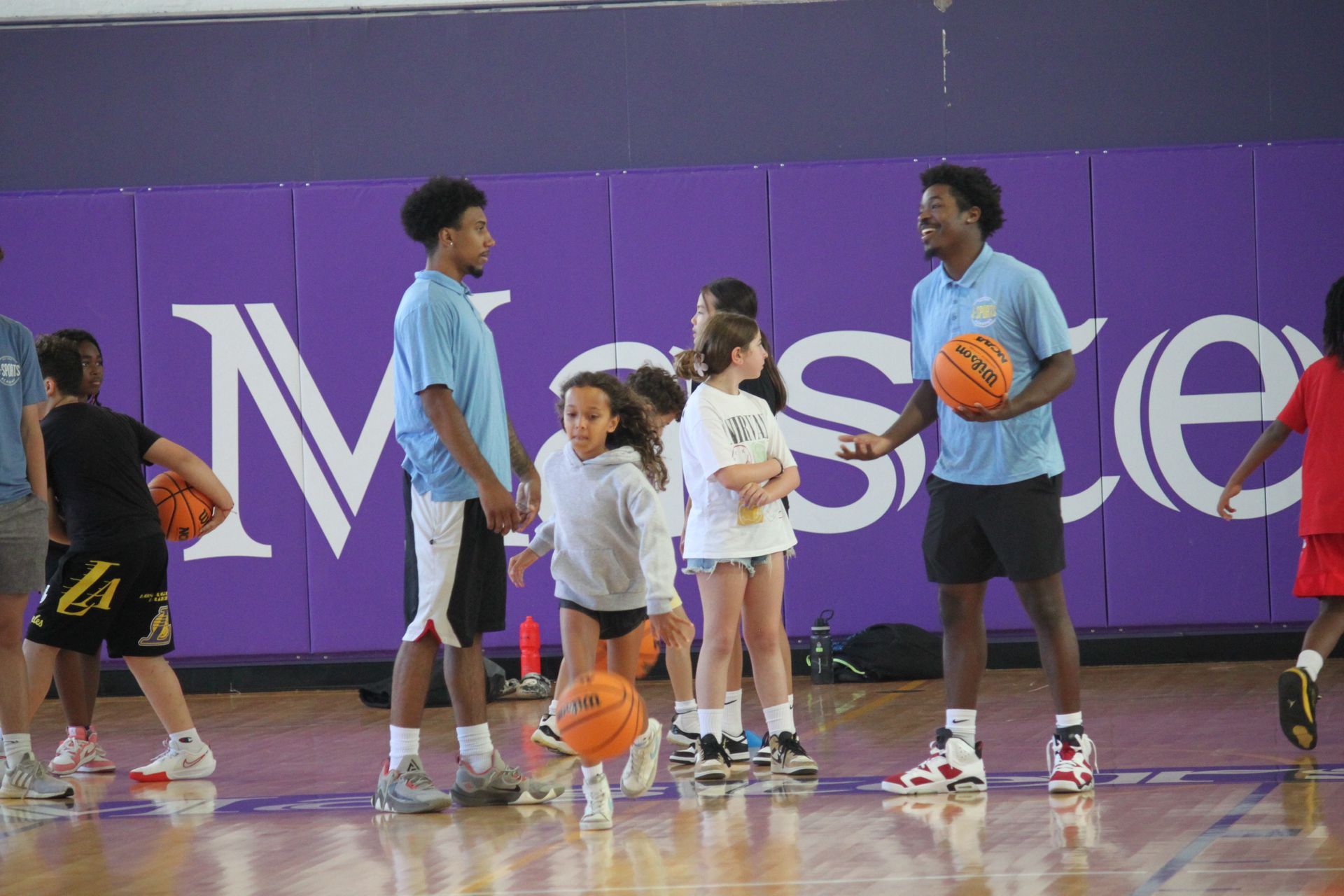 A group of children are playing basketball on a court in front of a wall that says messe