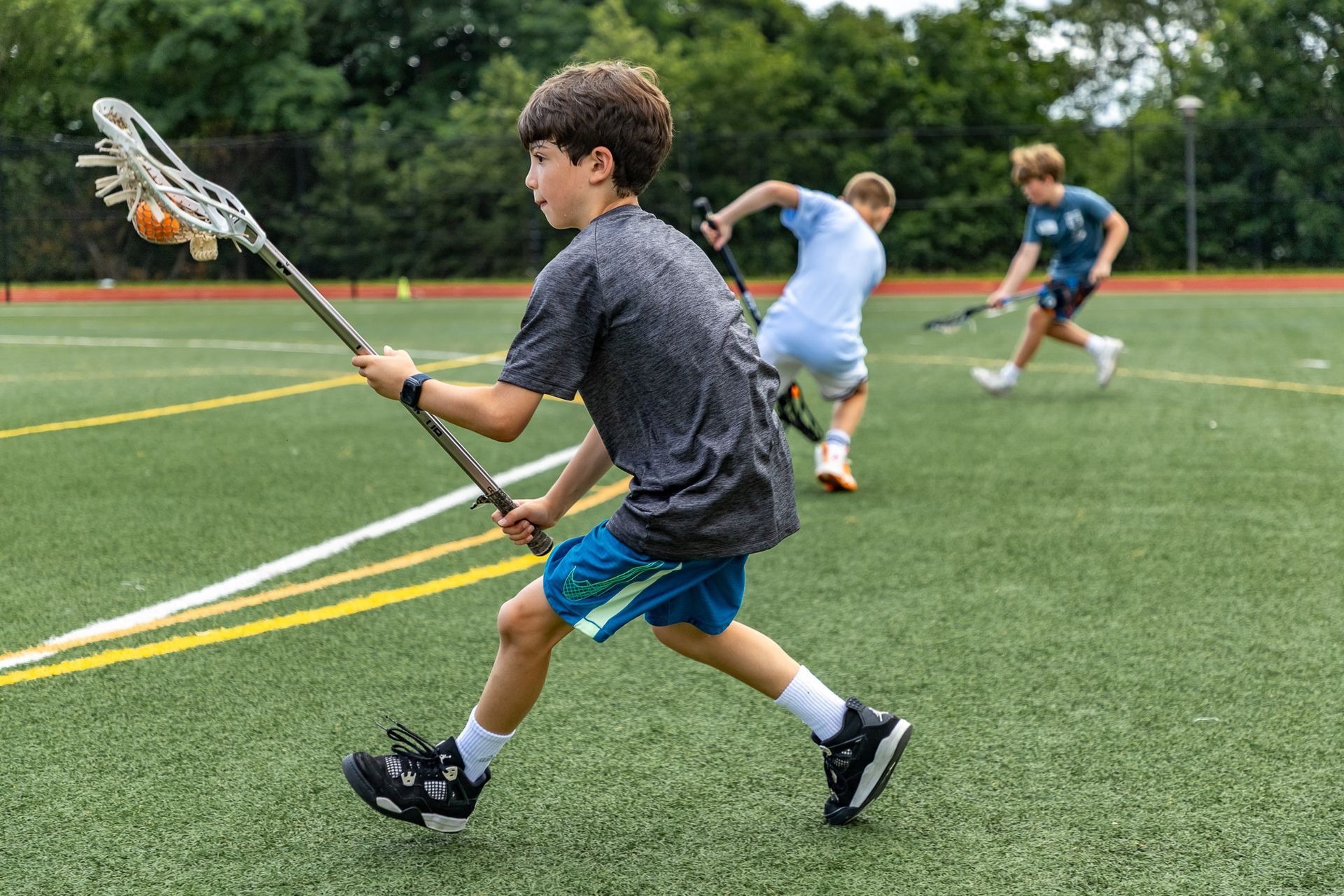 A young boy in a blue shirt is holding a lacrosse stick