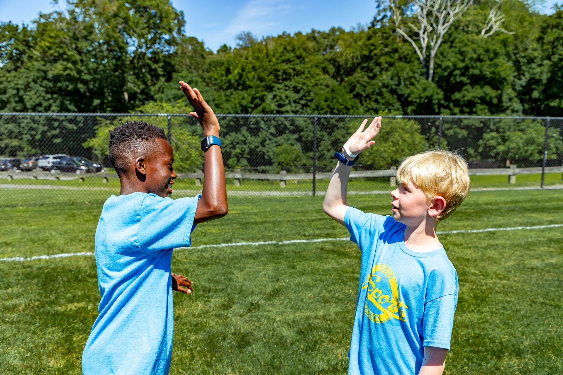 Two boys in blue shirts giving each other a high five on a grassy field.