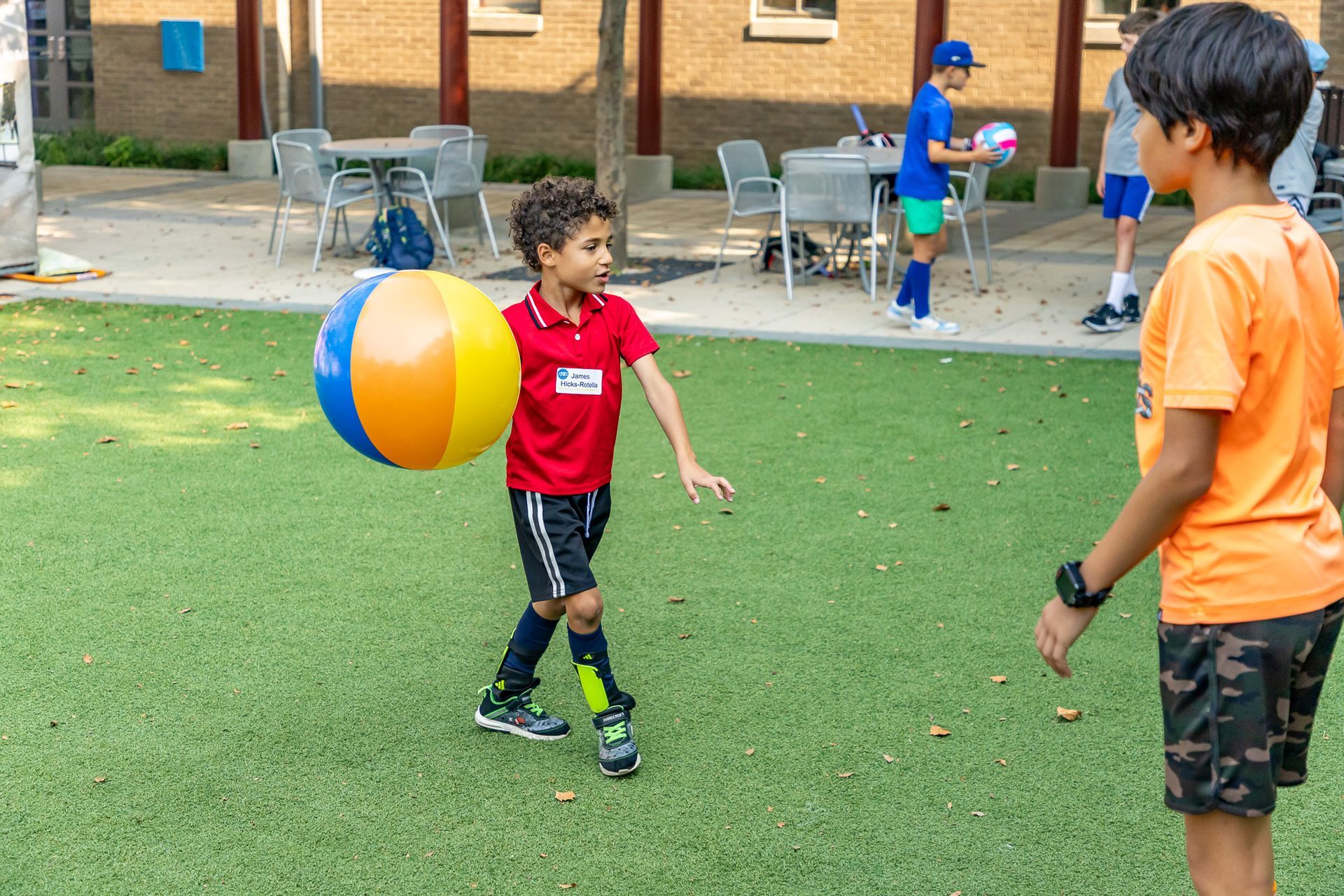 Boy in red holding a beach ball, preparing to throw to boy in orange on a green field.