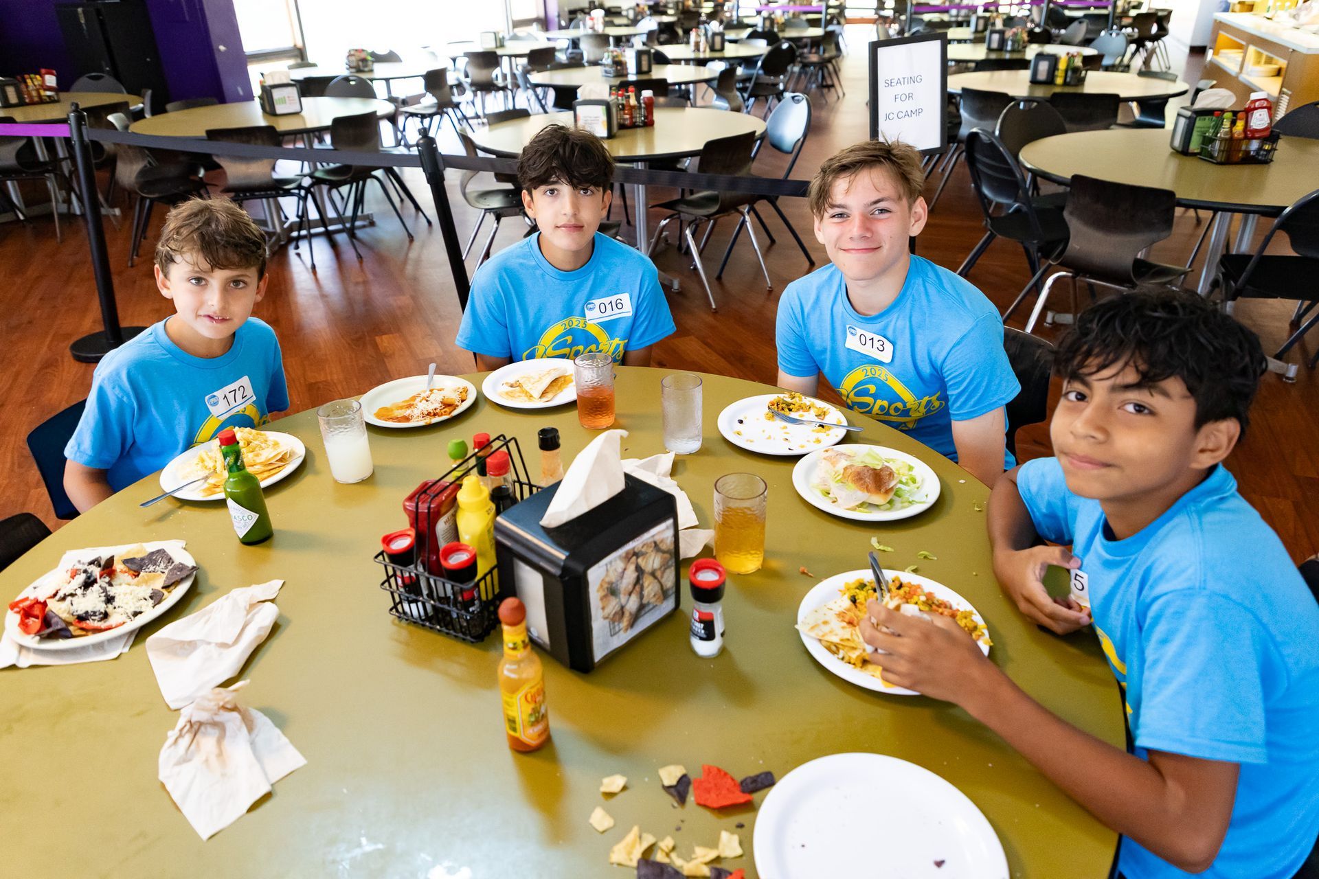 Four boys in blue shirts at a round table eating in a dining room.