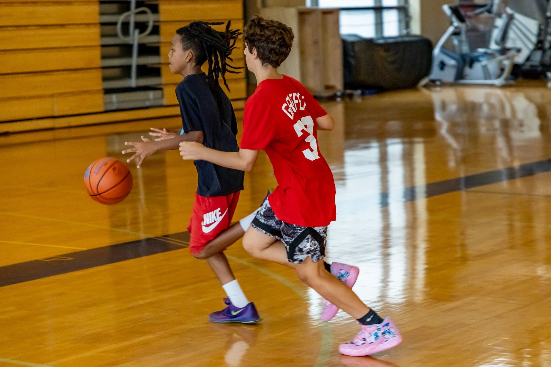 Two boys playing basketball on a wooden court; one dribbles, the other defends.