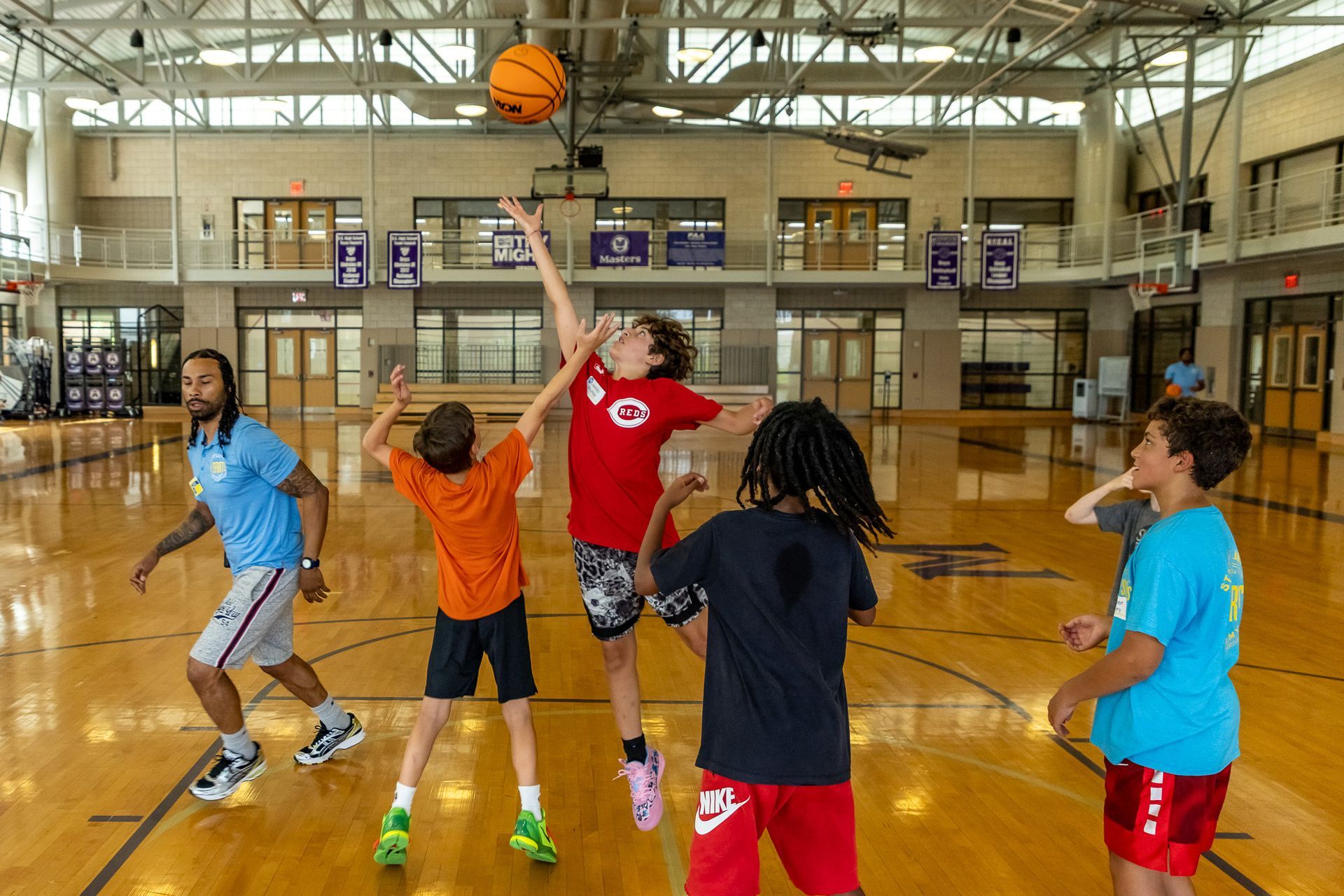 Basketball practice: Kids jumping for the ball in a gym, coach watches.
