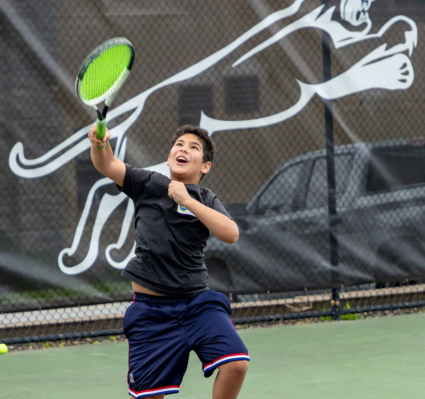Boy playing tennis, hitting the ball with a racket on a green court, smiling and athletic.