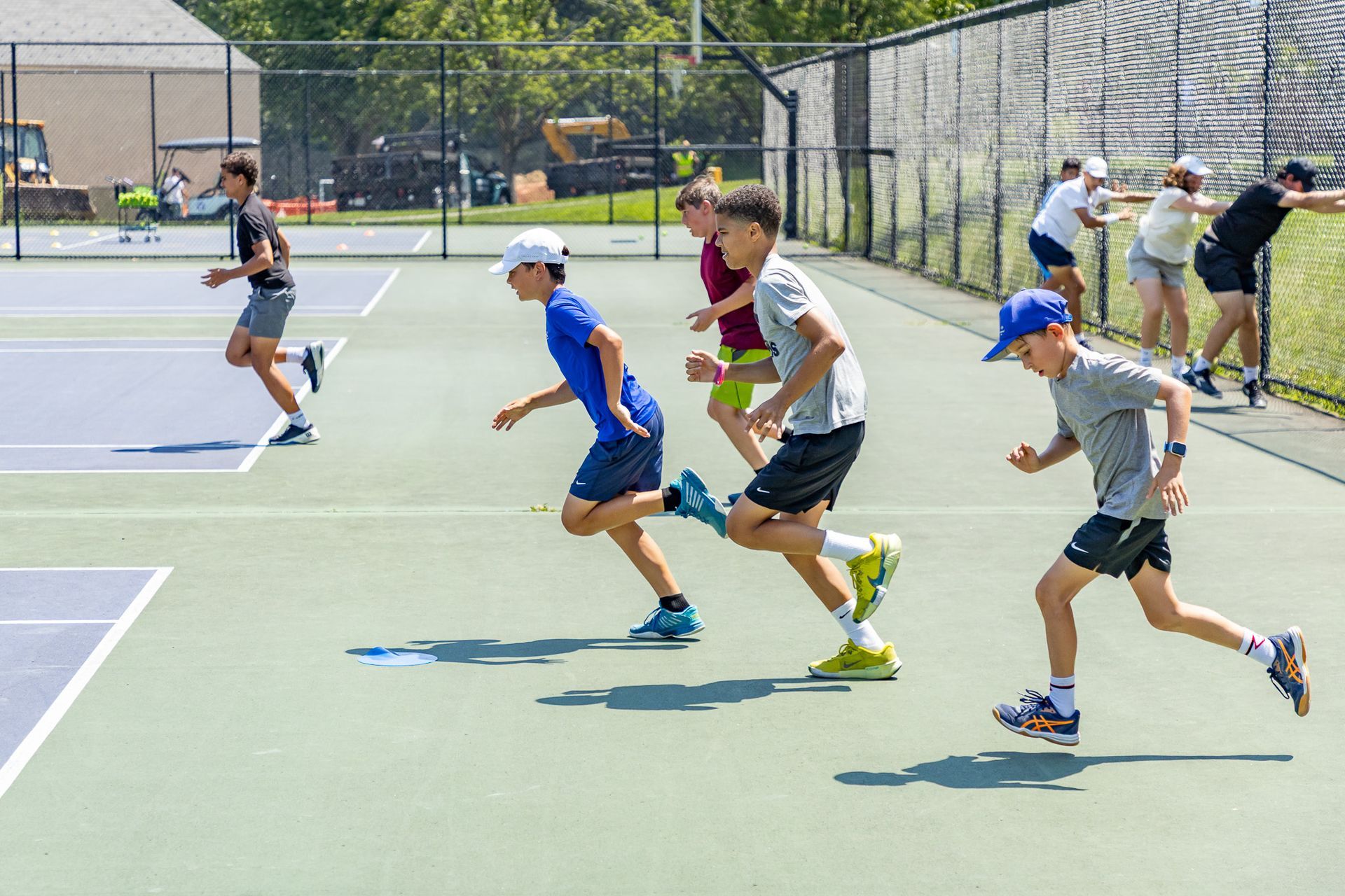 Group of boys running on a tennis court, some wearing hats.