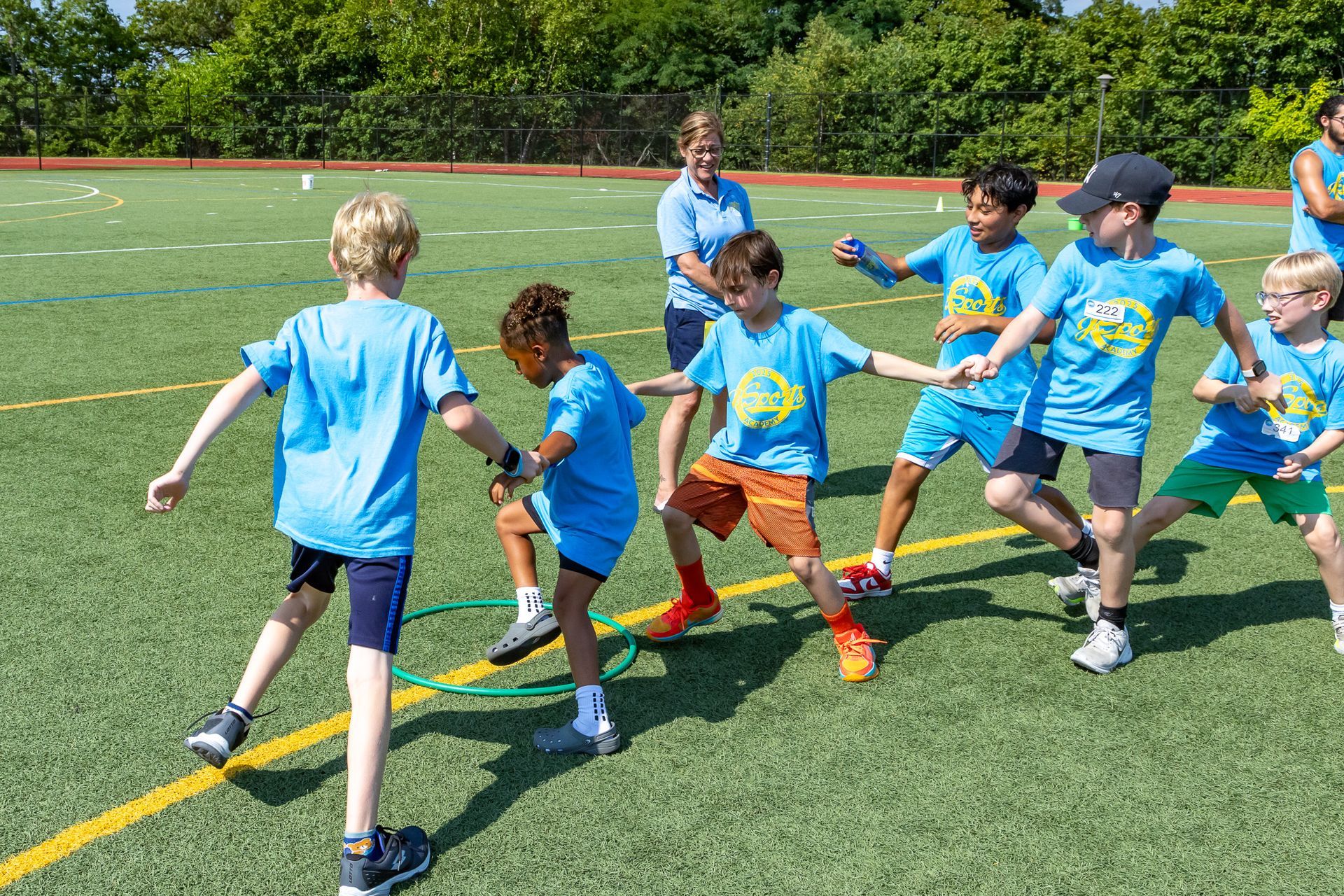 Children playing tug-of-war on a green field, supervised by an adult.