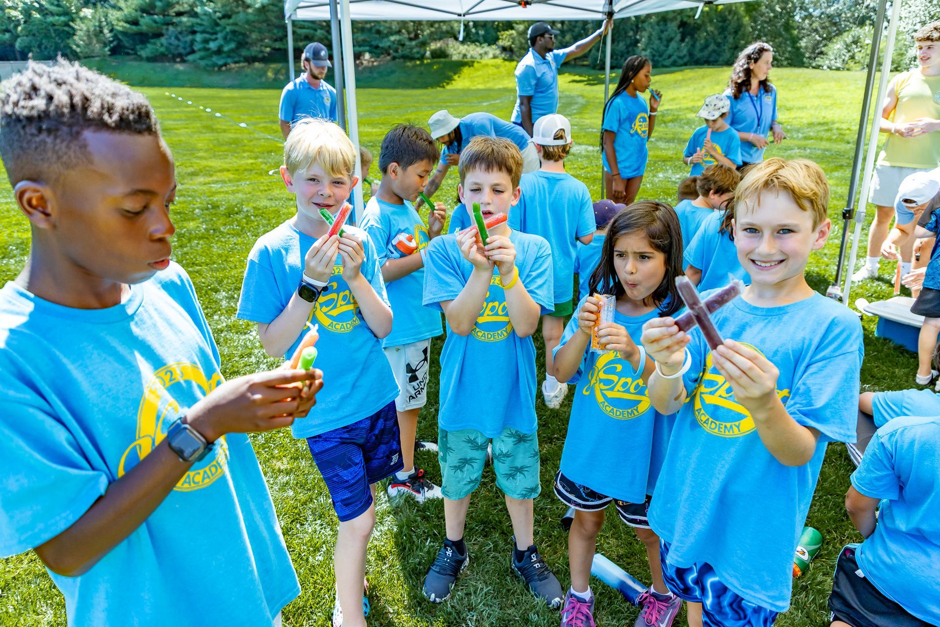 Kids in blue shirts holding crafts outside on a sunny day.