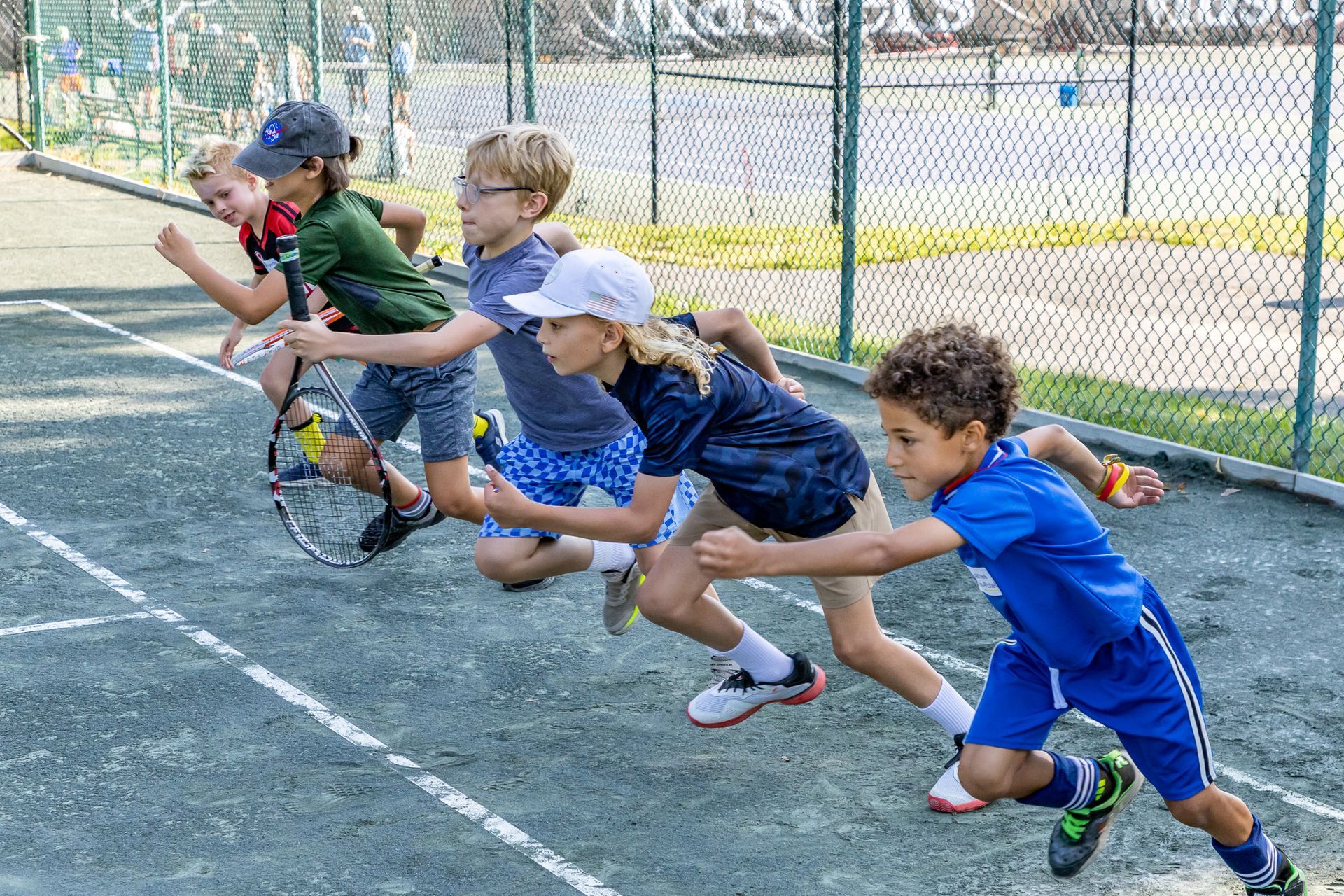 Five kids running on a tennis court, rackets in hand, ready to play.