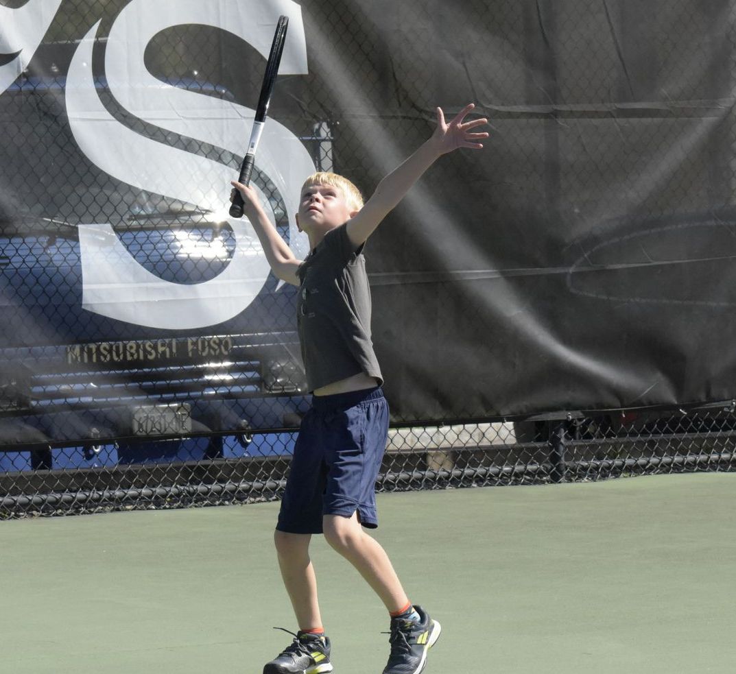 A young boy is playing tennis in front of a mitsubishi sign