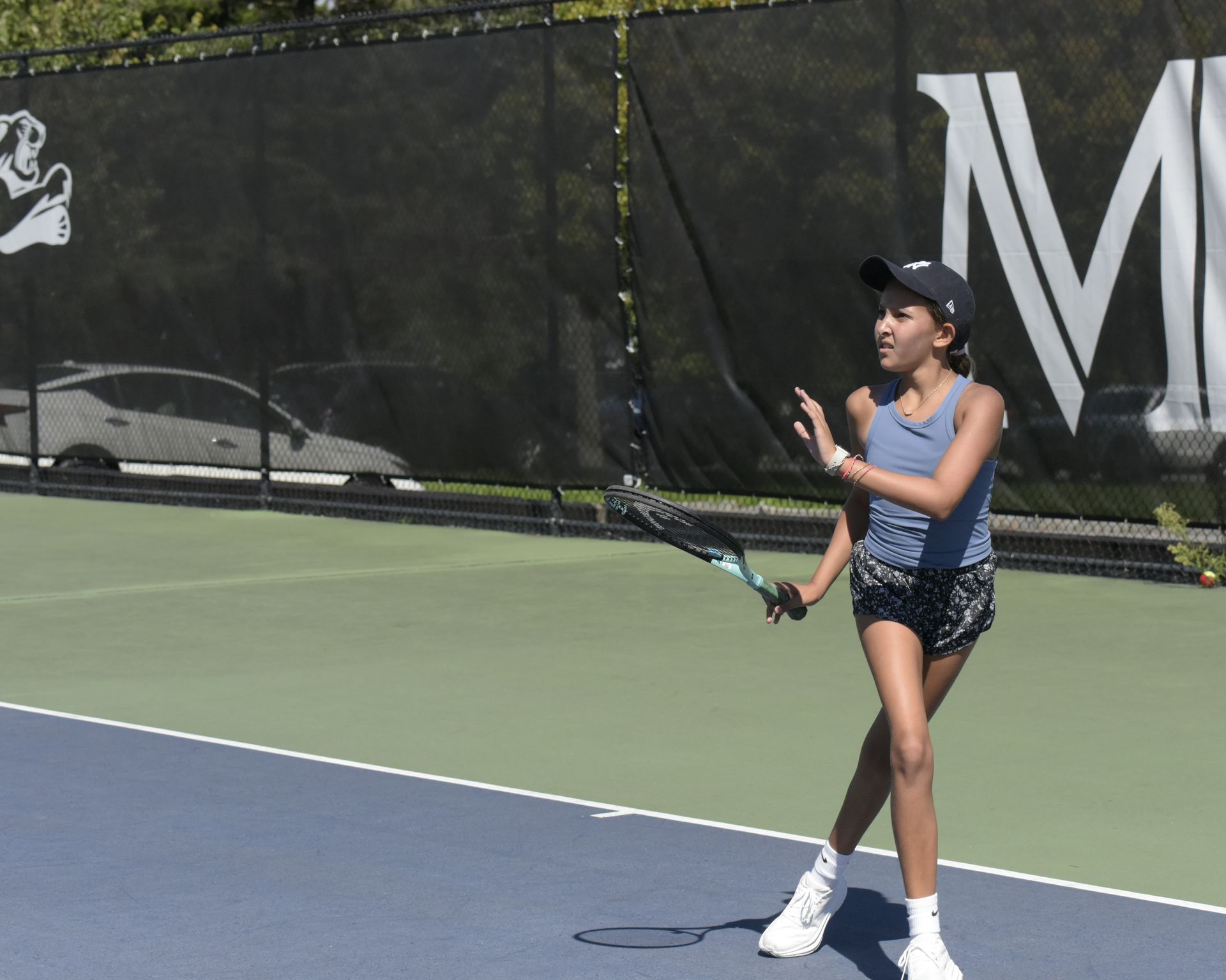 A girl is playing tennis on a court with the letter m behind her