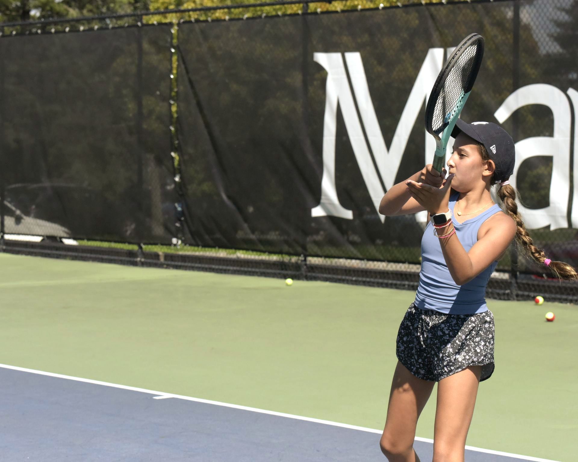 A girl is playing tennis in front of a sign that says ma