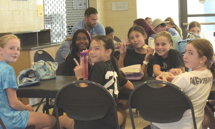 A group of young girls are sitting at tables in a cafeteria.