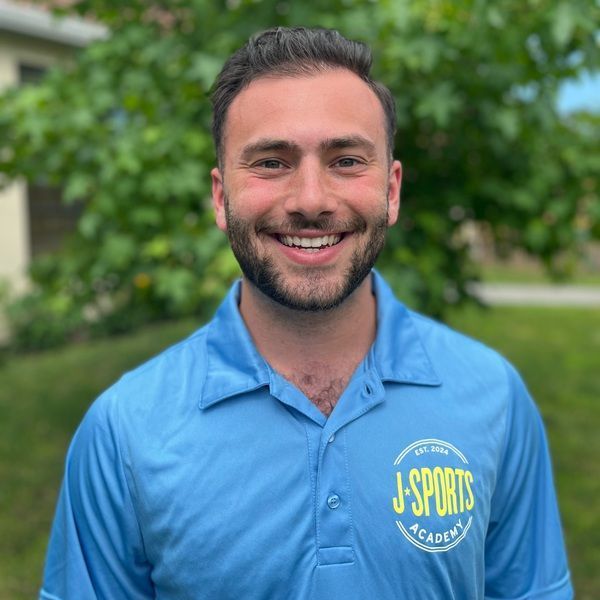 A man with a beard is wearing a blue shirt that says j-sports academy.