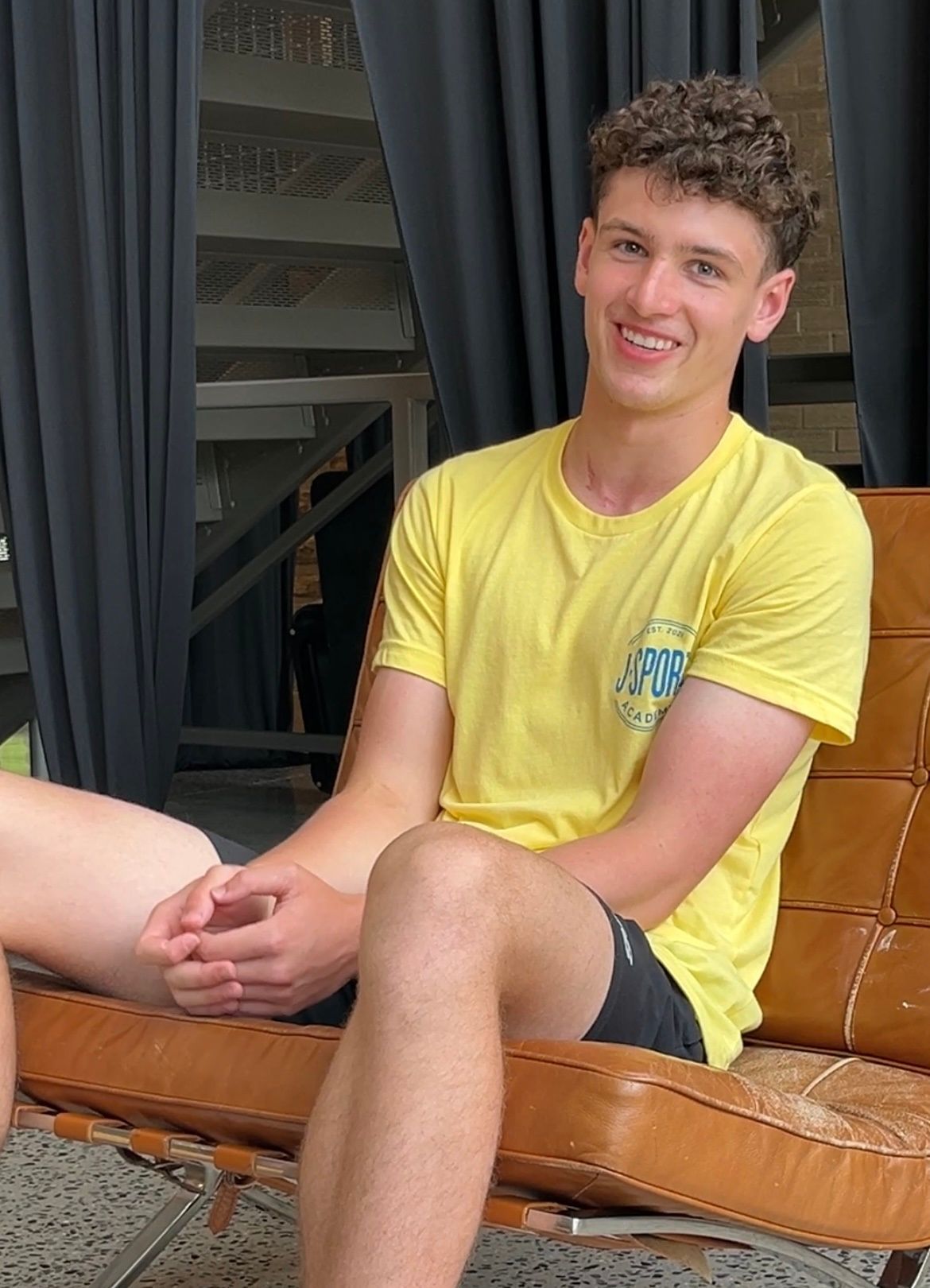 A young man in a yellow shirt is sitting on a chair.