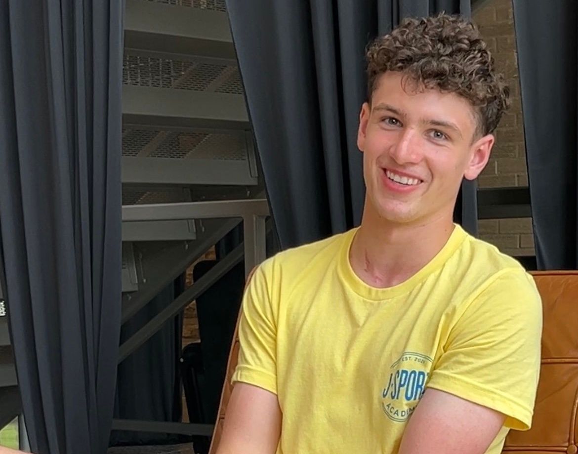 A young man in a yellow shirt is sitting on a chair.