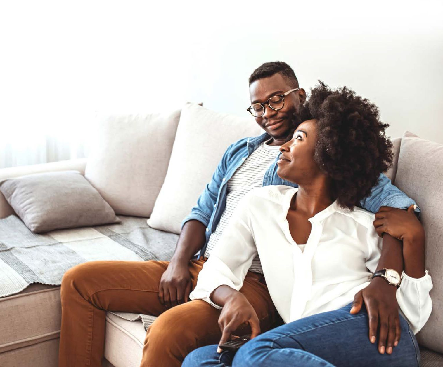 Couple sitting on a couch, smiling and chatting in a bright living room.