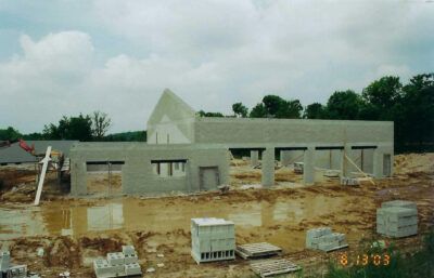 Building under construction with concrete block walls; muddy ground, cloudy sky. | Joe's Slinger Service