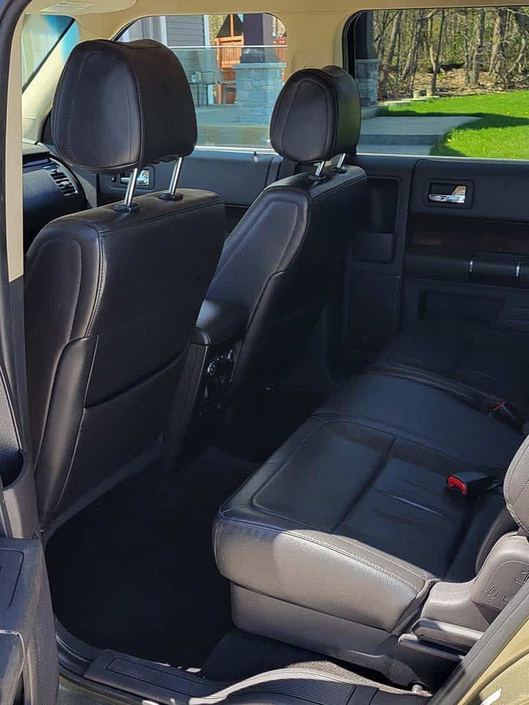 Rear interior of a black vehicle. Two rows of black leather seats. Bright daylight streams in from the side. | Joe's Slinger Service