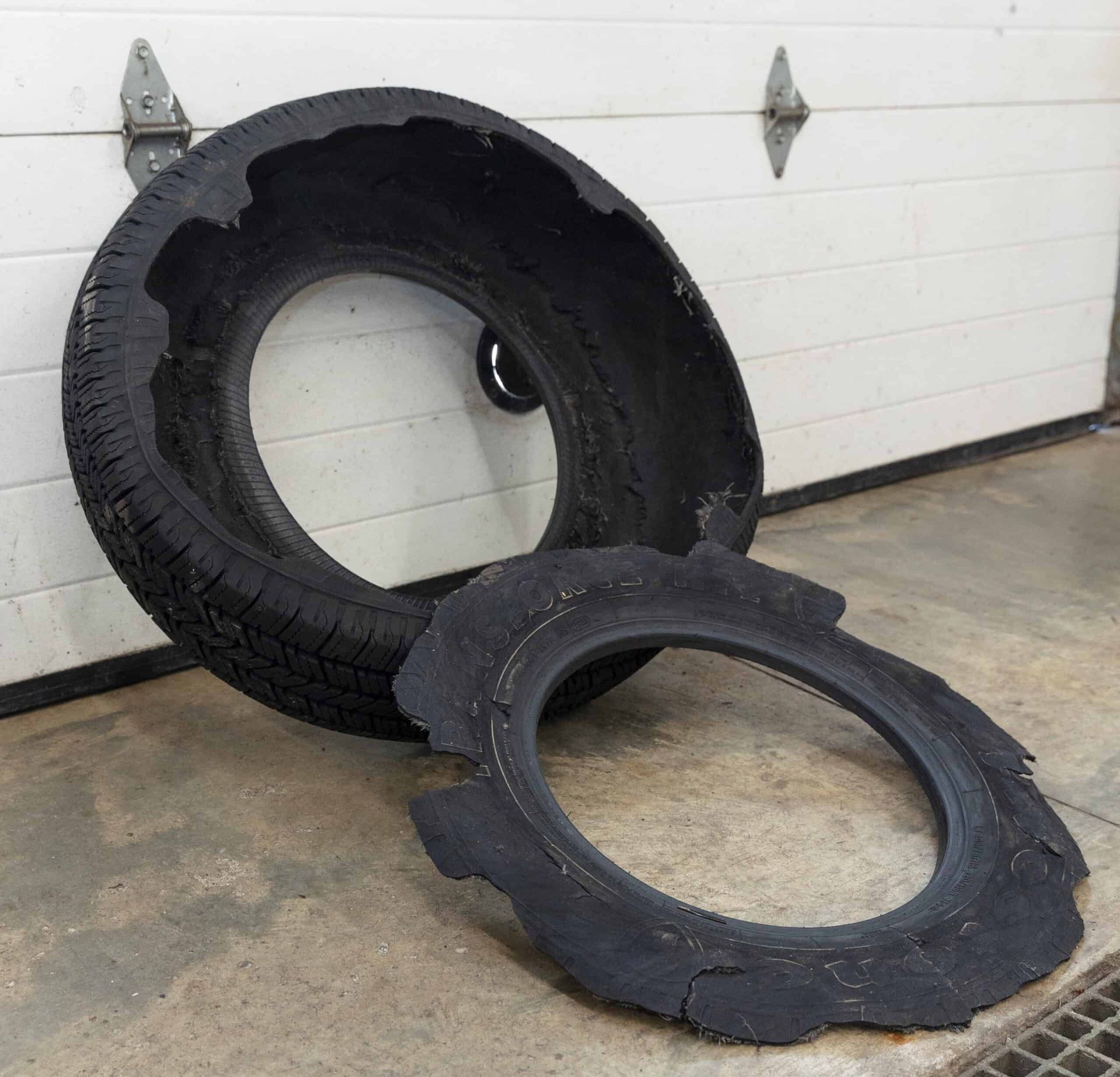 Damaged tire, split open, pieces lying on a concrete floor in front of a white garage door. | Joe's Slinger Service