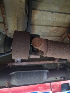 Undercarriage view: rusty driveshaft components, including a U-joint, a flange, and an exhaust pipe. | Joe's Slinger Service