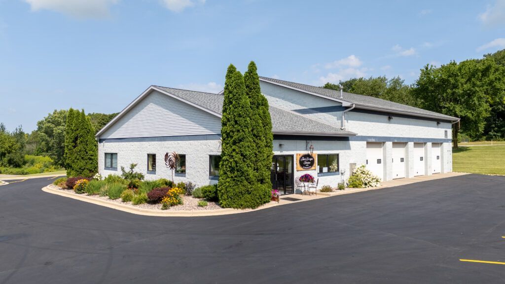 Exterior view of a light gray commercial building with landscaping and garage doors on a sunny day. | Joe's Slinger Service