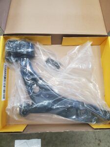 Black car suspension control arm in a cardboard box, wrapped in plastic. | Joe's Slinger Service
