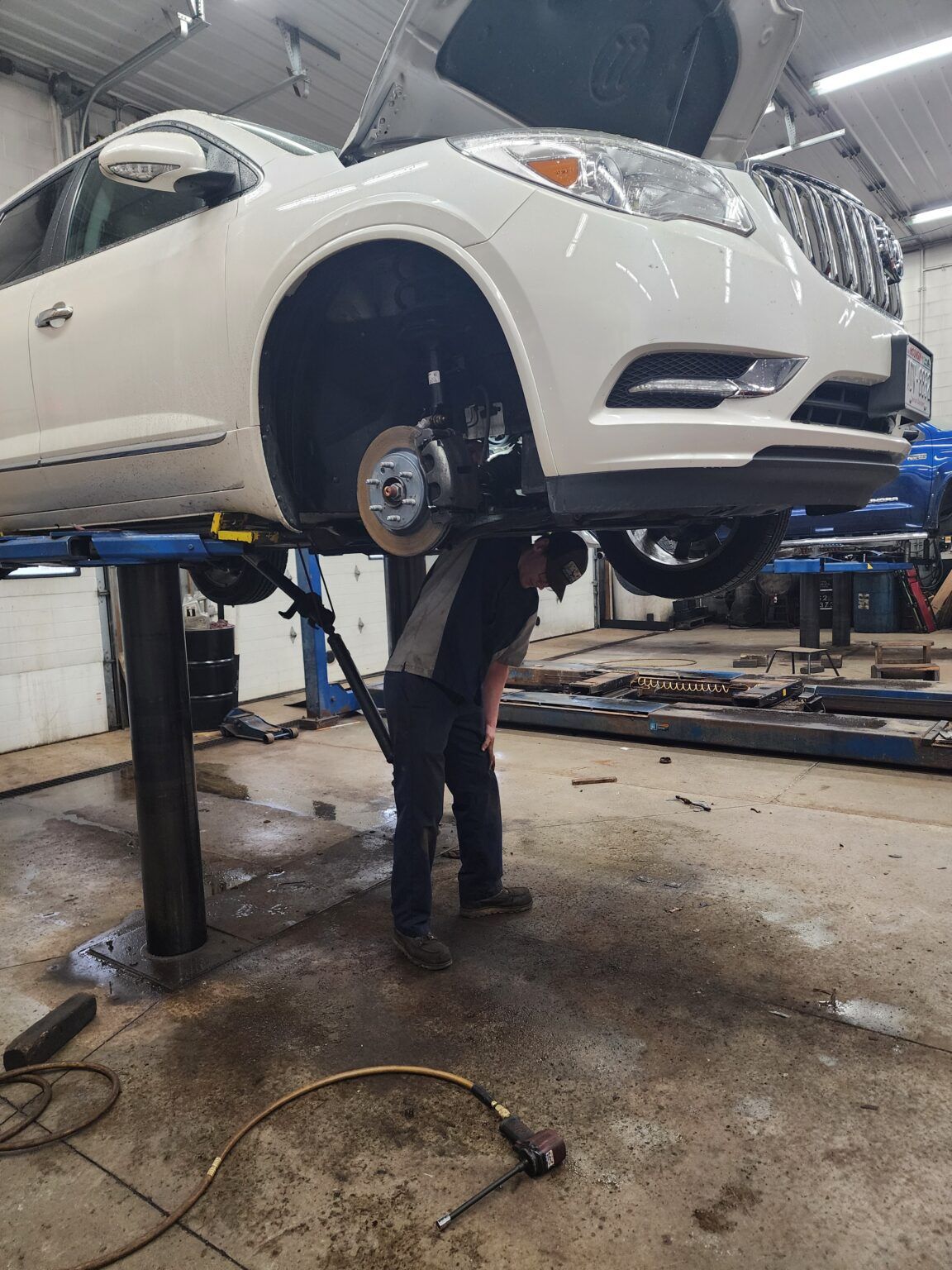 Mechanic working on the front wheel of a white SUV lifted on a vehicle hoist in a garage. | Joe's Slinger Service