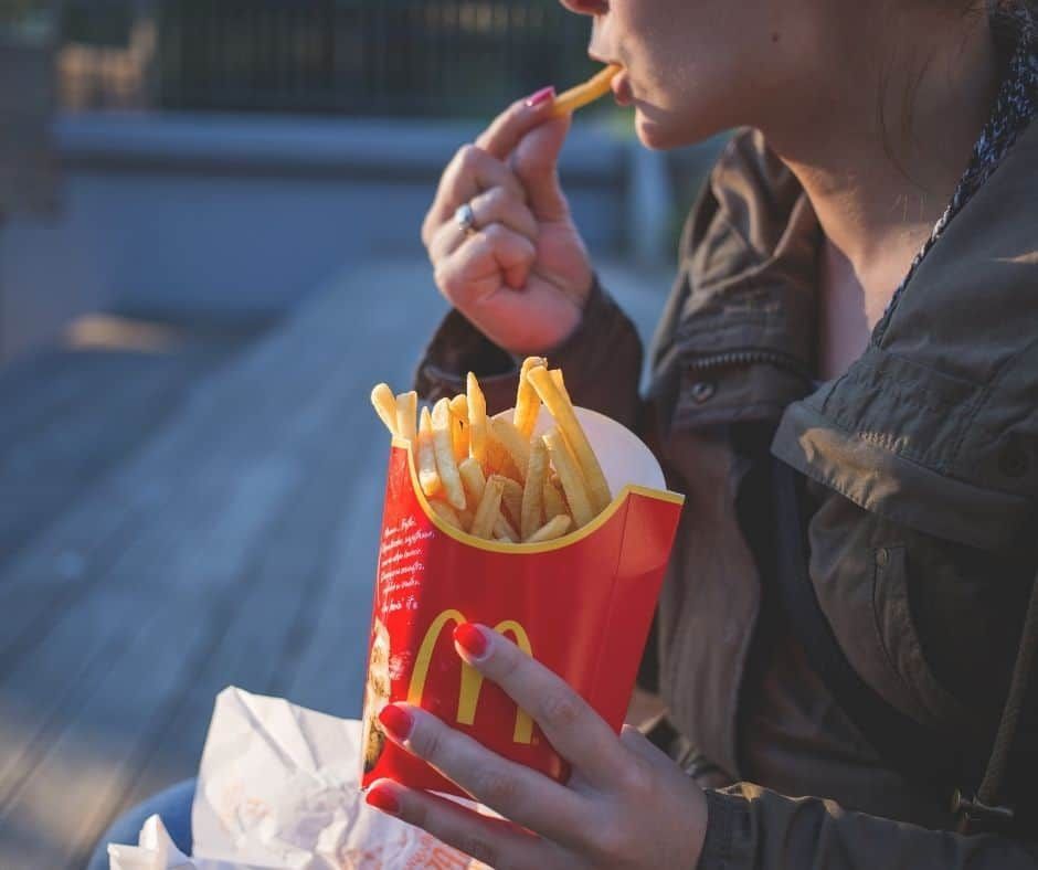 Woman eating French fries from a McDonald's container; red nails, outdoor setting. | Joe's Slinger Service