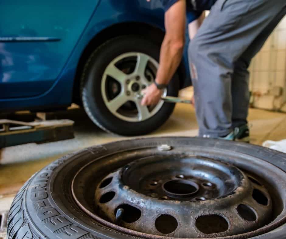 Mechanic changing a car tire with a wrench; blue car in a garage. | Joe's Slinger Service