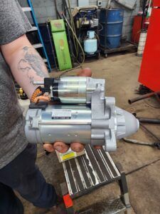 Person holding a new car starter motor in a garage setting. | Joe's Slinger Service