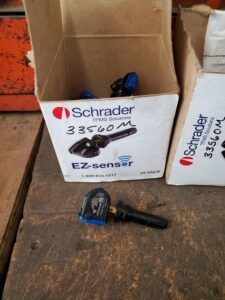 Boxes of Schrader EZ-sensor TPMS sensors; one sensor outside the boxes on a wooden surface. | Joe's Slinger Service