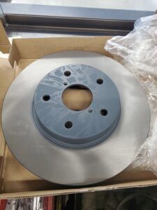 New brake rotor, silver disc with a gray hub, in a cardboard box. | Joe's Slinger Service
