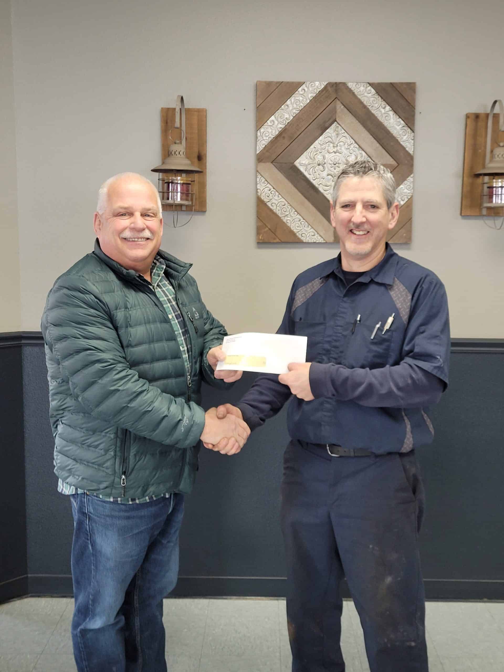 Two men shaking hands, one giving a check. Inside a building, art on the wall. | Joe's Slinger Service