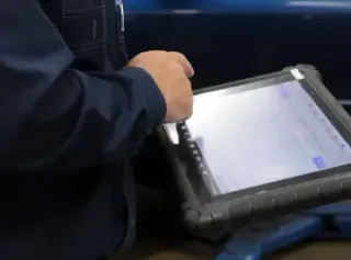 Person in blue workwear uses a tablet with a diagnostic program, presumably in a garage.