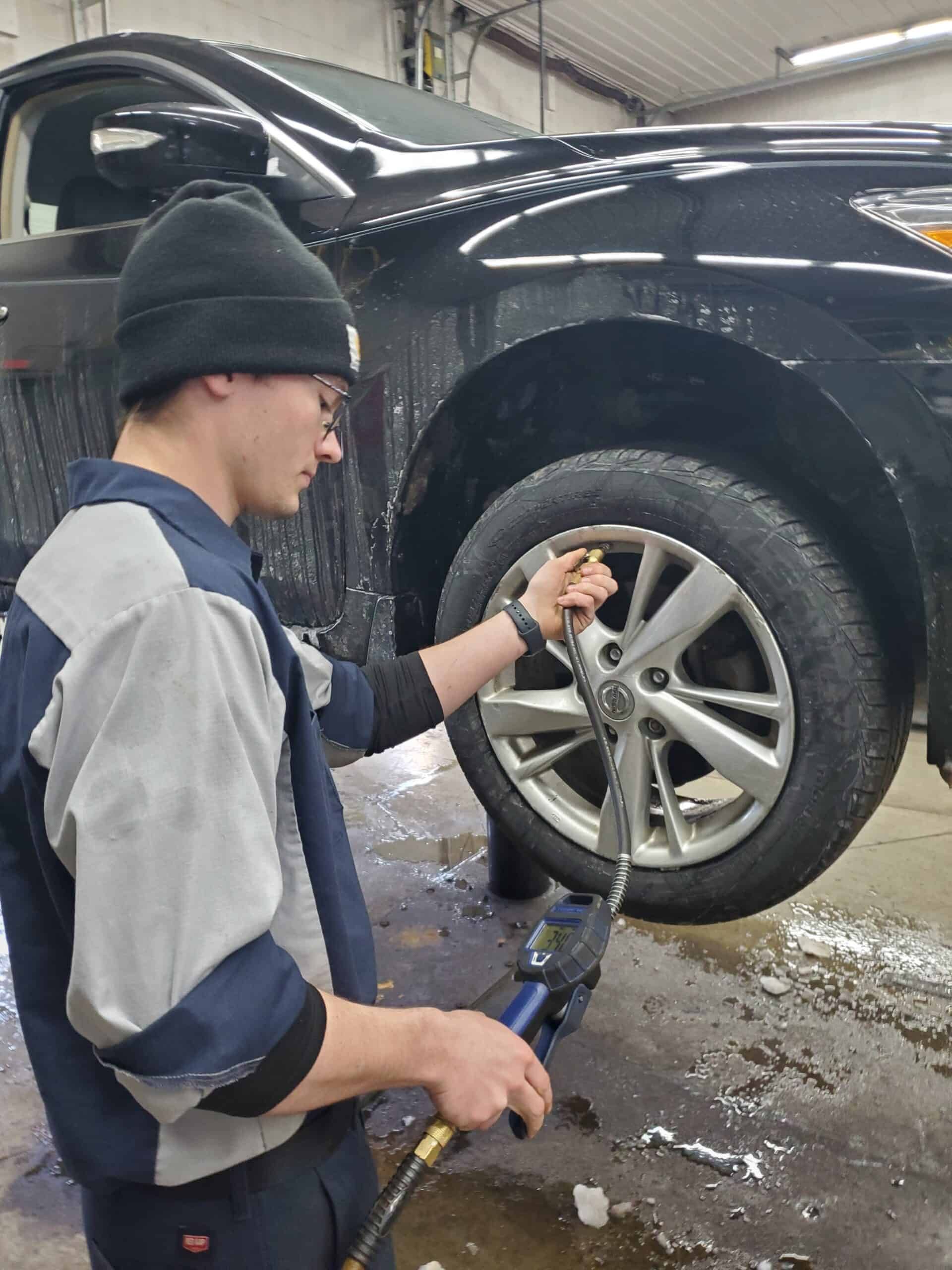 Mechanic tightening a lug nut on a car tire, wearing a work uniform and beanie in a garage. | Joe's Slinger Service