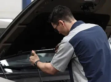 Mechanic working on a car engine, holding a tool under the open hood.