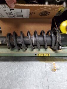 Black spring coil on a shock absorber, resting on a green surface. A box is in the background. | Joe's Slinger Service