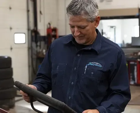 Mechanic in blue work shirt examines steering wheel in a garage.