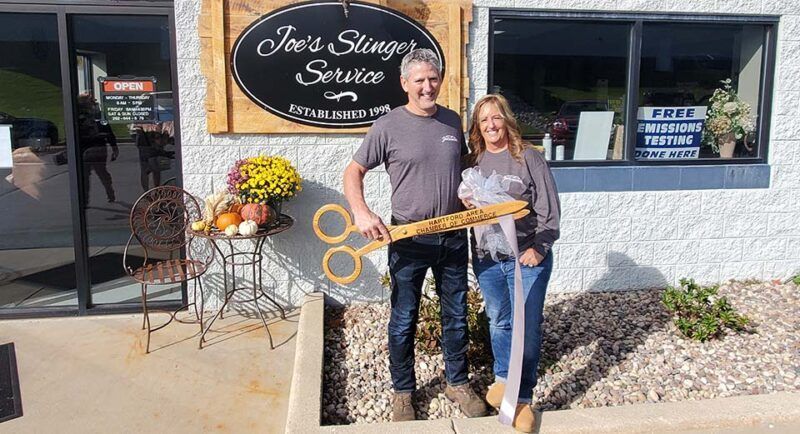 Man and woman hold giant scissors in front of a business, 