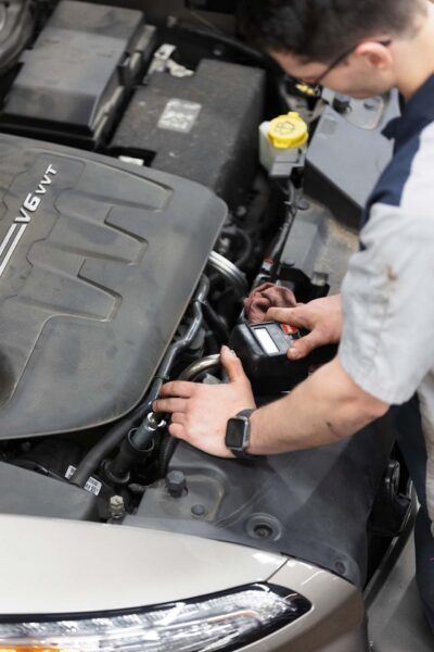 Mechanic working on a car engine; holding a tool. Engine bay is open. | Joe's Slinger Service