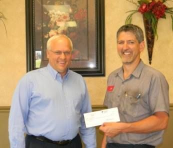 Two men, one in a blue shirt, the other in a work shirt, stand indoors. The second man holds a check. | Joe's Slinger Service