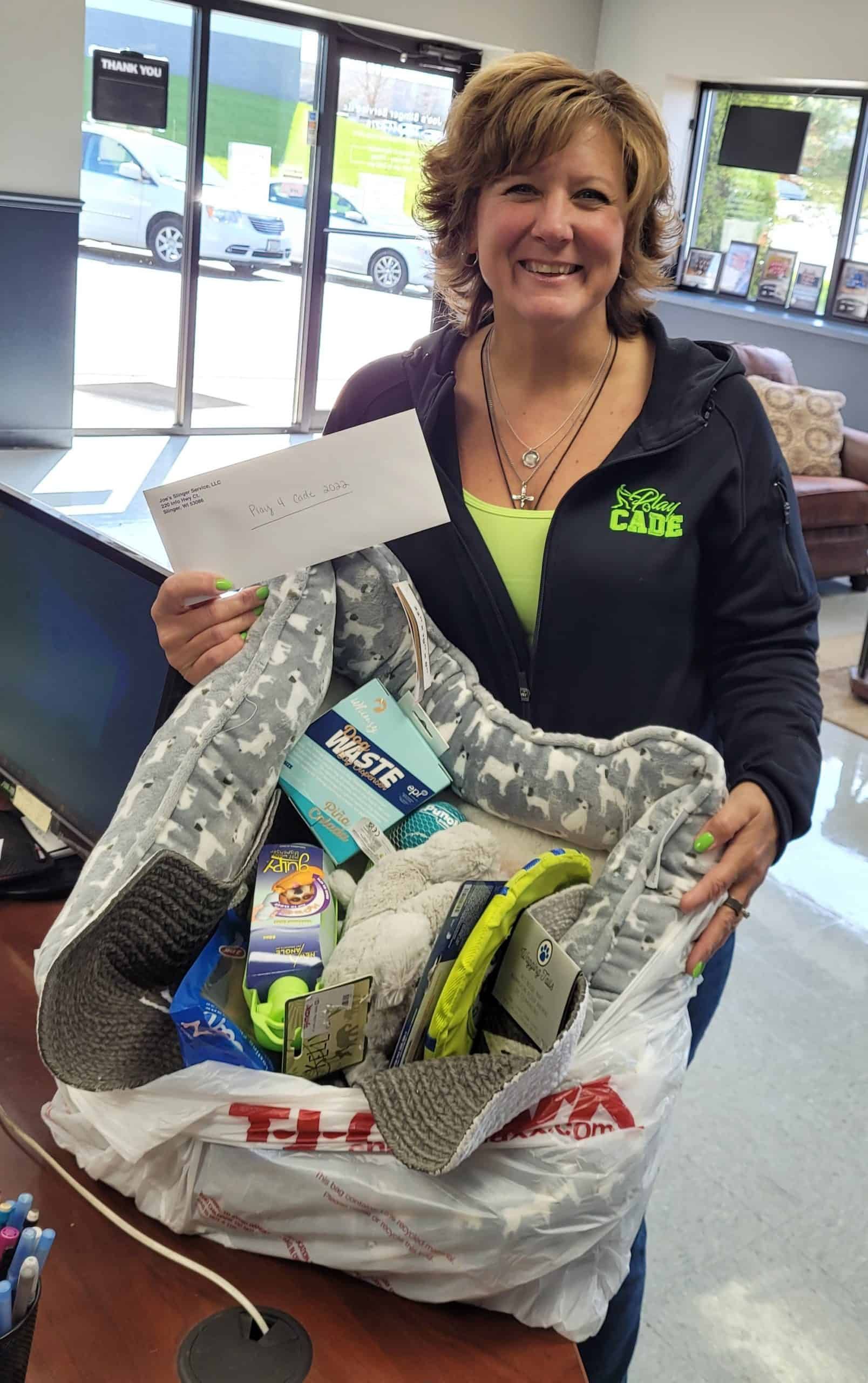 Woman holding a gift bag and an envelope. Smiling, wearing a green shirt, in a store with vehicles visible. | Joe's Slinger Service