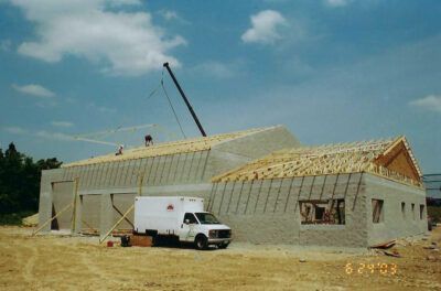Construction of a light gray concrete building with wooden roof framing, under a blue sky. Crane and white truck present. | Joe's Slinger Service