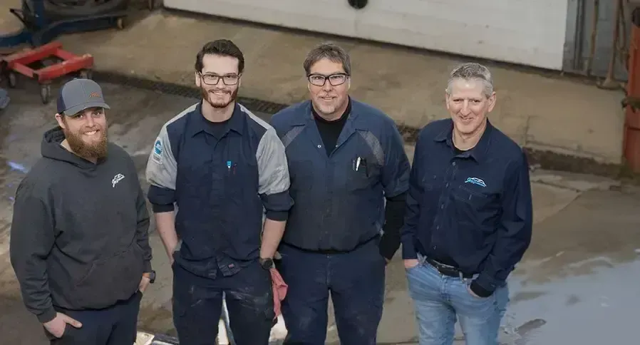 Five technicians stand together indoors; smiling, wearing shop attire | Joe's Slinger Service, LLC