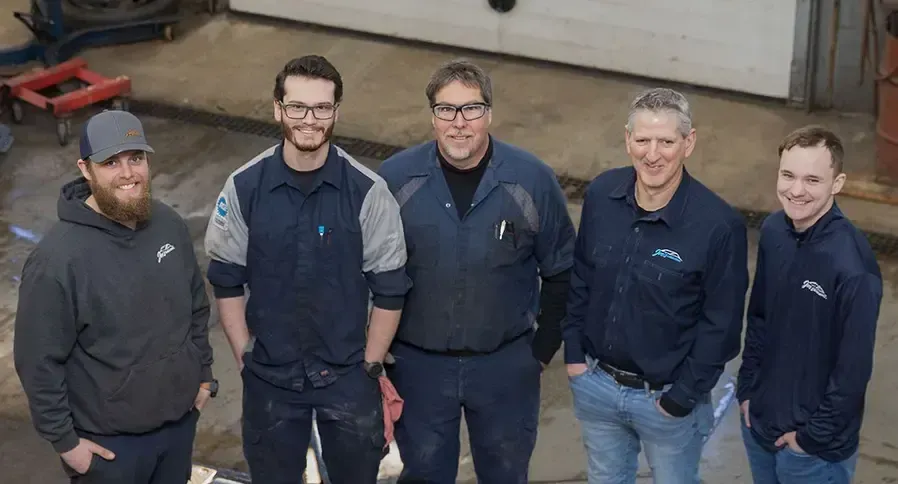 Five technicians stand together indoors; smiling, wearing shop attire | Joe's Slinger Service, LLC